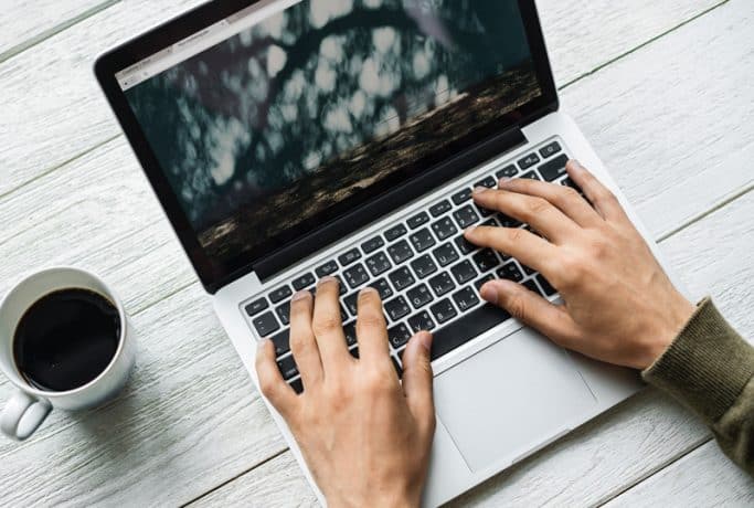 A top-down view photograph of someone typing on a laptop, with a cup of coffee beside them.