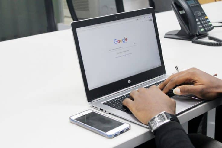 A man typing at a laptop computer, open to the Google search bar home page.