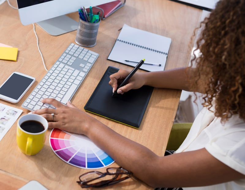 A graphic designer works at a tablet with a color palette beside her.