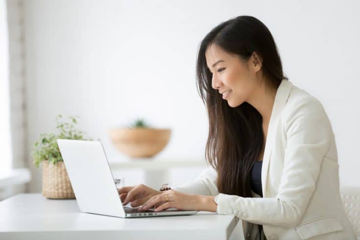 woman typing on a laptop on a white desk next to plants