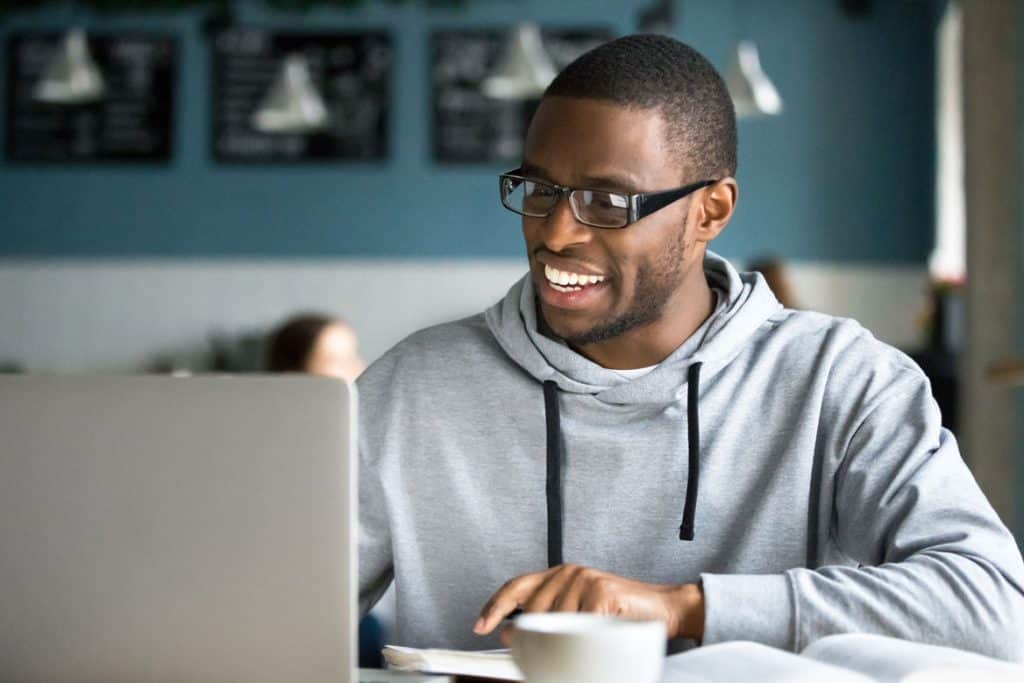 man in sweatshirt working on a laptop and drinking tea at a coffee shop