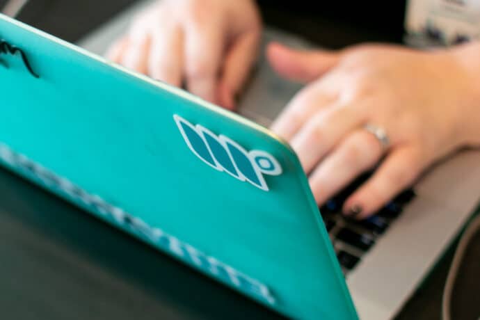 someone typing on laptop with a teal cover and mediavine stickers