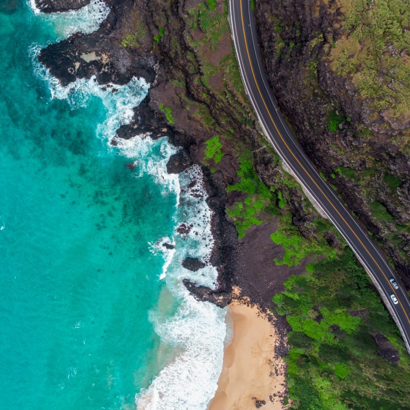 aerial view of a road next to a beach with clear blue waters