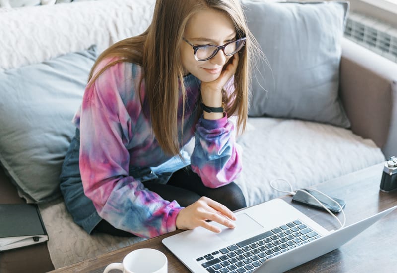 A woman using a laptop computer while sitting on a love seat.