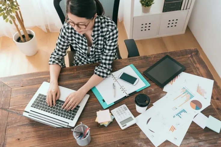 woman typing on a laptop at a desk with papers on it 