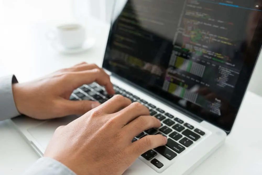 hands typing on a laptop with code on a black screen