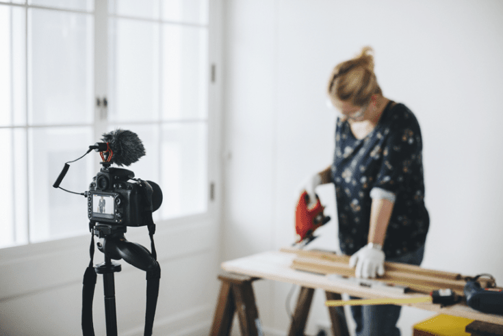 A woman vlogging a DIY, holding a jig saw.