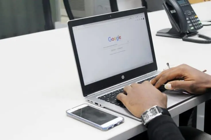 A man typing at a laptop computer, open to the Google search bar home page.
