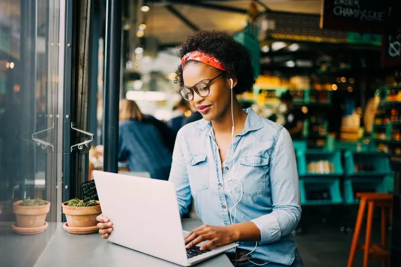 woman wearing earbuds and a denim shirt sitting at a counter with a laptop