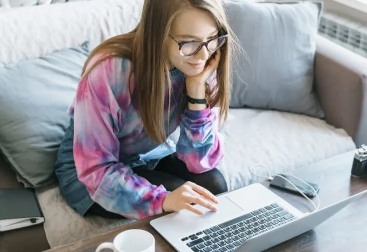 A woman sitting on a love seat, blogging on a laptop computer.